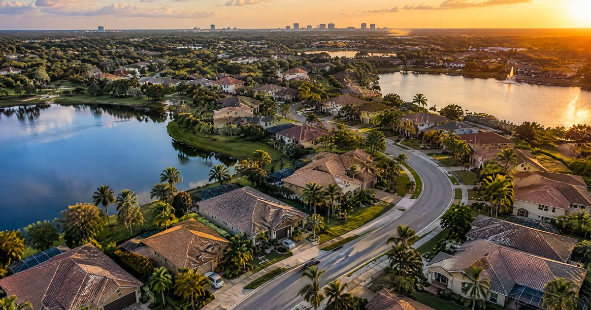 Aerial view of a Central Florida neighborhood with tile-roof homes, palm trees and lakes at sunset